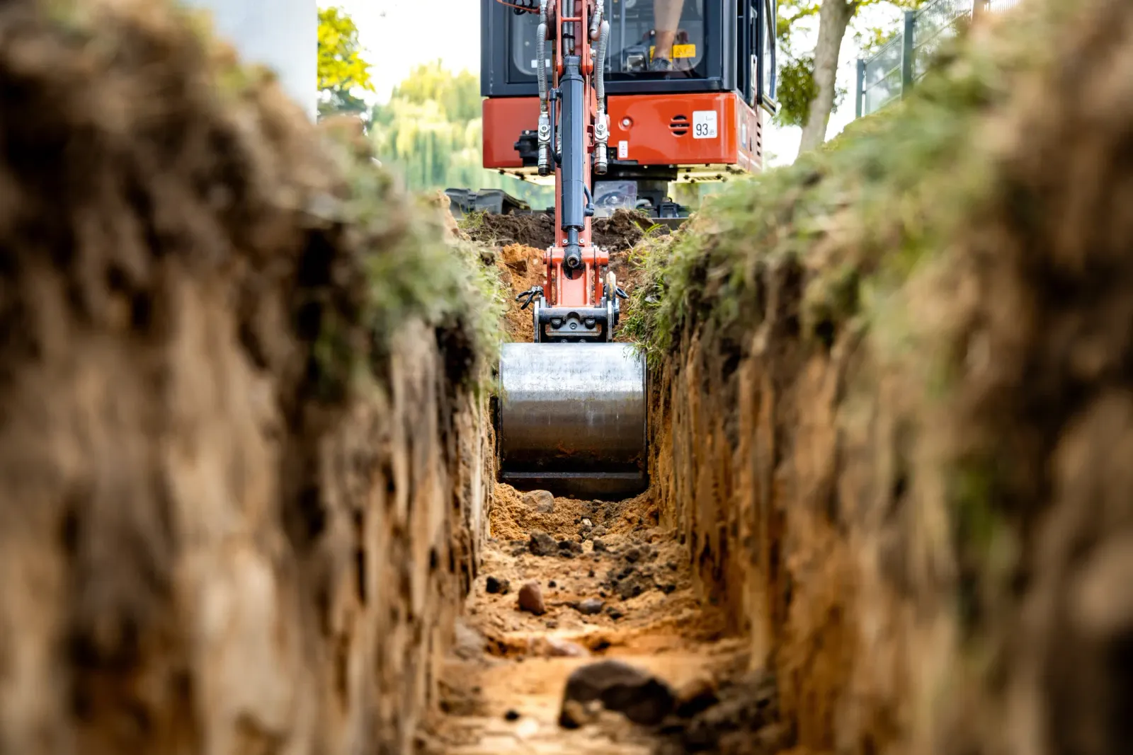A mini excavator lowering a large pipe into an excavated trench, illustrative of residential septic excavation work