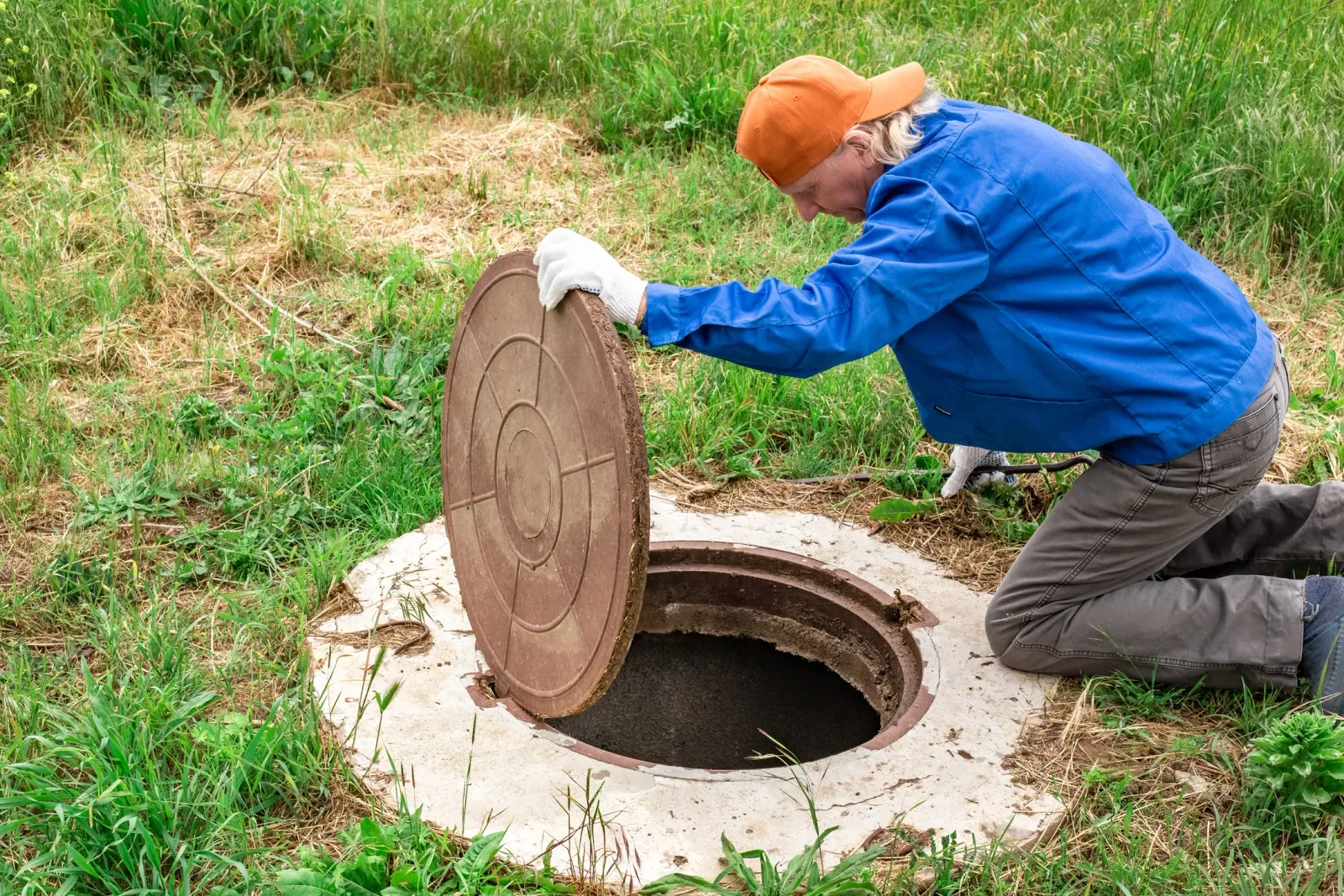 A septic service technician opening a tank access lid in a grassy yard — illustrative stock photo of septic tank service, not an actual Flagstaff-area job site